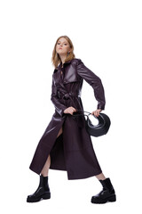 Fototapeta premium High fashion photo of a beautiful elegant young woman in pretty long purple lilac leather jacket, coat, handbag posing on white background. Slim figure. Blonde