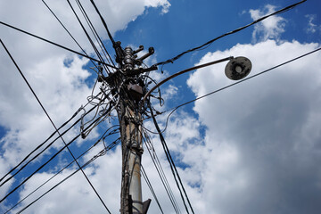 A busy utility pole with numerous wires and a streetlight against a blue sky