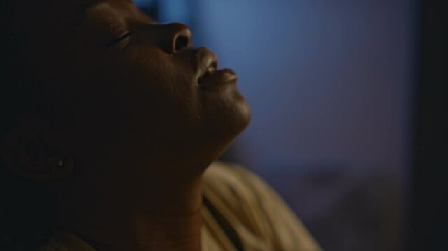 Side closeup of young African American woman trying to calm down and breathing deeply while having sleep disorder from traumatic flashbacks at night, ptsd