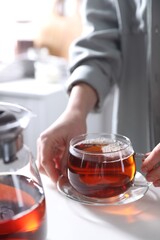 Woman with cup of hot tea at white table, closeup