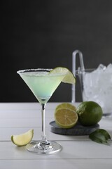 Delicious Margarita cocktail in glass and limes on white wooden table