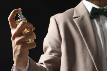 Man spraying luxury perfume on dark background, closeup