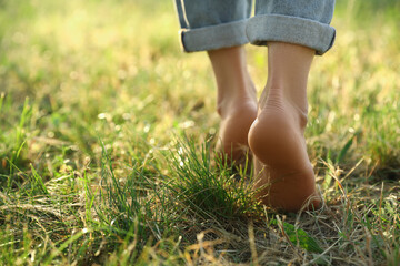 Woman walking barefoot on green grass outdoors, closeup. Space for text