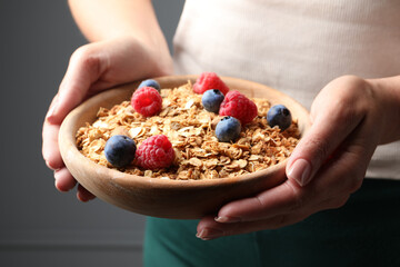 Woman holding bowl of tasty granola with berries and nuts on dark grey background, closeup
