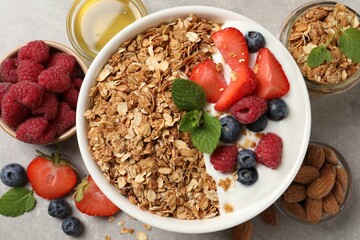 Tasty granola with berries and yogurt in bowl on grey textured table, flat lay