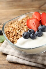 Tasty granola with berries and yogurt in bowl on wooden table, closeup