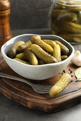 Pickled cucumbers in bowl, fork and spices on grey table