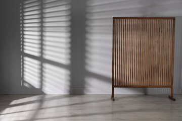 Wooden folding screen near light wall indoors, space for text