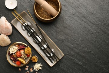 Incense sticks, Tibetan singing bowl, stones, dry flowers and candle on black table, flat lay. Space for text
