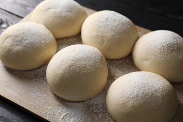 Raw dough balls on black wooden table, closeup
