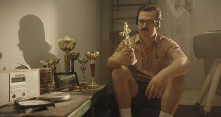 Athlete Reflects on Sports Trophies in Vintage Gym Setting