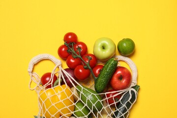 Delivery of vegetarian products. String bag with different vegetables and fruits on yellow...