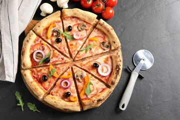 Cut delicious vegetarian pizza, cutter and ingredients on black table, flat lay