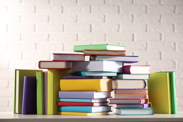 Stacks of many colorful books on white wooden table against brick wall