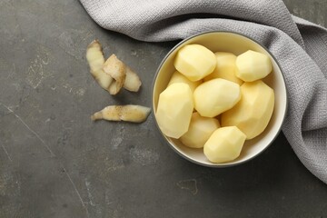 Fresh raw potatoes in bowl and peels on grey table, top view. Space for text