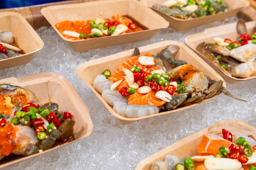 Thai strret food on night market. Selection of marinated raw seafood dishes made of salmon, shrimps and crabs prepared for sashimi. Asian food in Bangkok, Thailand. Japanese and Korean cuisine
