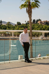 Hombre joven con traje y camisa en sitio lujoso con mar.  Business man. Trabajando con tablet y móvil. 