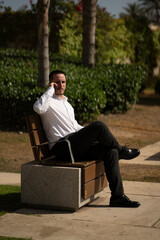 Hombre joven con traje y camisa en sitio lujoso con mar.  Business man. Trabajando con tablet y m&oacute;vil.  Sentado en un banco llamando por tel&eacute;fono.