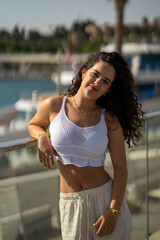 Chica joven en verano sonriendo haciendo fotos con el móvil en un lugar de mar y bonito. Pelo rizado y brillante. 