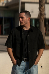 Chico joven modelo frente al mar y barco. Hombre con estilo informal. Ropa vaquera y negro.