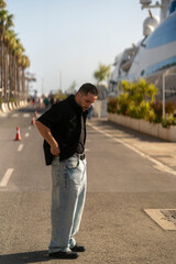 Chico joven modelo frente al mar y barco. Hombre con estilo informal. Ropa vaquera y negro.