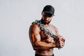 Naklejka premium Young strong man bodybuilder with heavy chain on white wall background