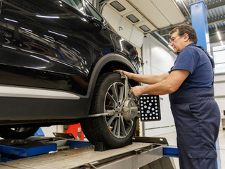 Auto mechanic sets the car for diagnostics and configuration. Wheel alignment equipment on a car...