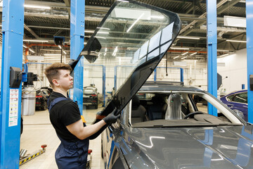 A mechanic at a car service center replaces a broken windshield on a SUV. Auto glass repair and windshield replacement