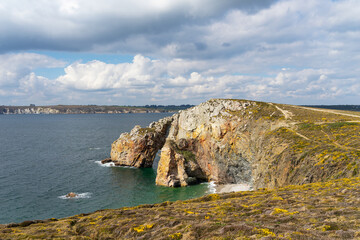 Les eaux turquoises de la mer d'Iroise scintillent au pied des falaises, sous un ciel nuageux, sur...