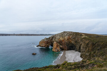 Les eaux turquoises de la mer d'Iroise scintillent au pied des falaises, sous un ciel couvert, sur la presqu'île de Crozon en Bretagne.