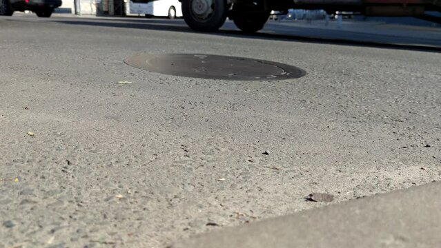 Close-up low angle view of cars driving on road surface in city in a sunny summer day. Rush hour traffic flow. Focus on the foreground. Slow motion video. Urban transport theme.
