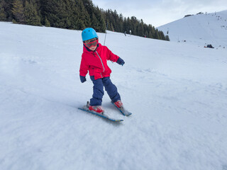 Young child learn to ski in snowy mountains, do first descent