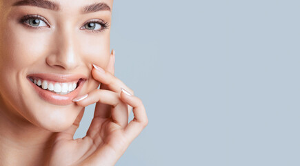 A close-up photograph of a woman with her hand resting on her cheek, showing a bright, white smile....