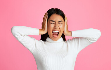 Asian young woman with her hands over her ears, screaming with her eyes closed. She is posing...