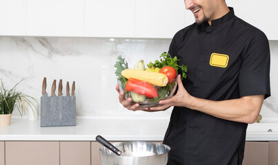 Close up of male hands holding a bowl full of fruits and vegetables in the kitchen. Healthy food concept	