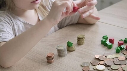 small child 4 years old playing with cash, house model on stacks euro currency coins, pocket money, concept home mortgage, home insurance, financial literacy of children, personal savings