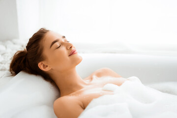 Relaxed woman enjoying hot bath with foam, resting with closed eyes, free space