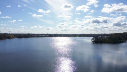 Drone view of a small lake in low sun surrounded by fields and woods.