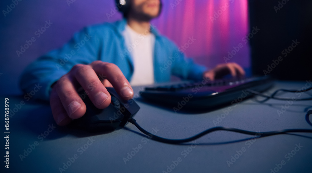 Poster a close-up view of a gamers hand gripping a wired computer mouse, with the keyboard and a blurred fi