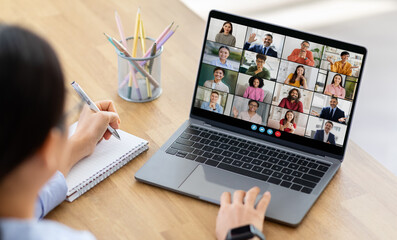 Lady woman sits at a desk, taking notes with a pen and notepad as she participates in a virtual...