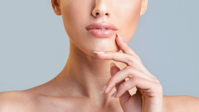 This image is a close-up shot of a woman face and hand. Her hand is resting on her chin, and her lips are slightly parted. The background is a light blue color, cropped