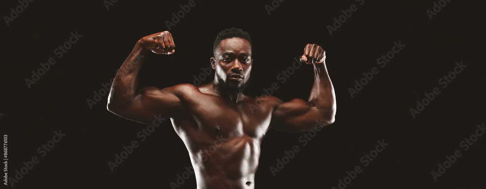 Wall mural A shirtless, muscular man flexing his biceps against a black background.