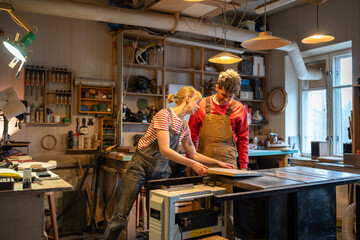 Serious married couple working together in carpentry shop. Attentive spouses engaged in joint small business for manufacture of joinery, making creating wooden products. Man and woman at workshop.