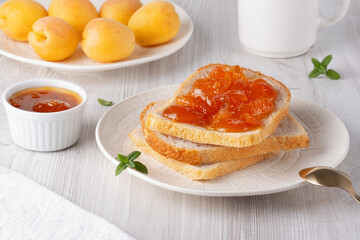 Apricot jam on bread in a white plate and a jar of apricot jam