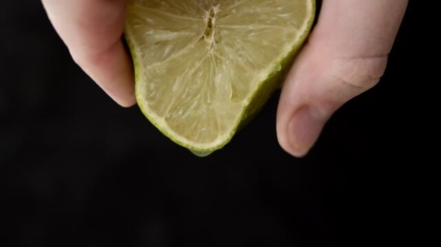 Squeezing green lime juice. Close Up on male hand extracting juice from a green lime half.