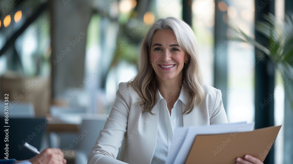 Canvas Prints A woman in a white jacket is smiling and holding a folder. She is sitting at a table in a restaurant