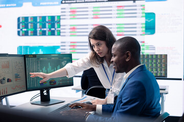 Diverse teammates examining statistics and infographics on computer in control room, joining forces...