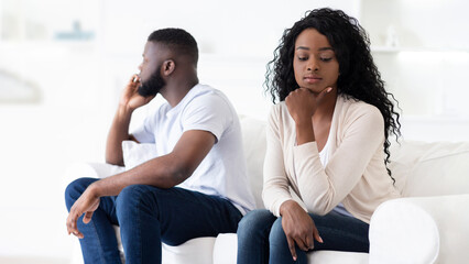 A couple sits on a white couch, facing away from each other, seemingly in disagreement.