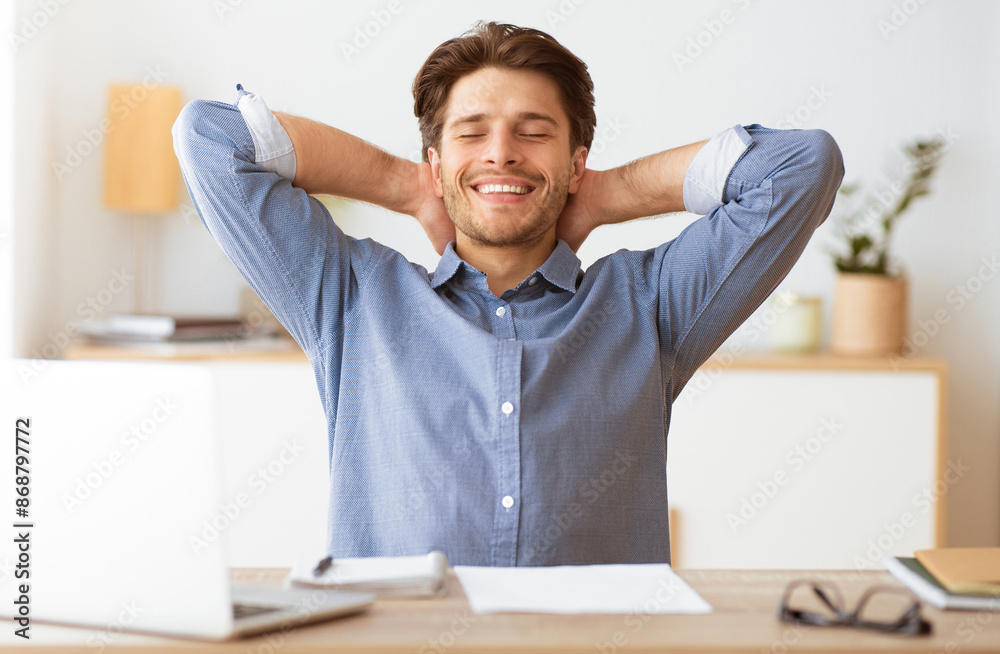 Poster a relaxed man sits at his desk, leaning back with his arms behind his head, smiling and taking a bre