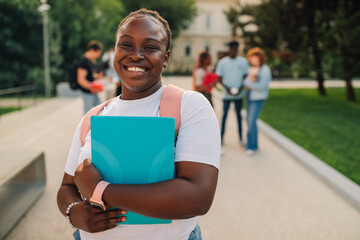 Portrait of diverse female student with textbook at campus smiling.